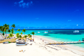 Aerial drone view of beautiful atlantic tropical beach with palms, straw umbrellas and boats. Bavaro, Punta Cana, Dominican Republic. Vacation background. - obrazy, fototapety, plakaty