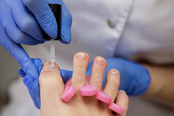 The nail technician covers the toenails with a colorless top coat. Aesthetic pedicure in the salon.