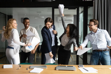 Overjoyed happy young and senior multiracial diverse business people colleagues celebrating corporate success, workday finish or closing profitable deal, dancing and having fun together in office.