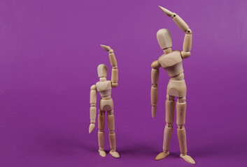 Two wooden puppets are doing aerobics exercise on a purple background. Healthy lifestyle concept