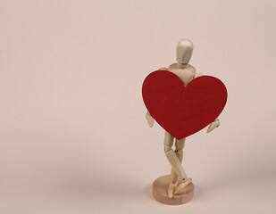 Wooden puppet mannequin holding red heart on beige background.