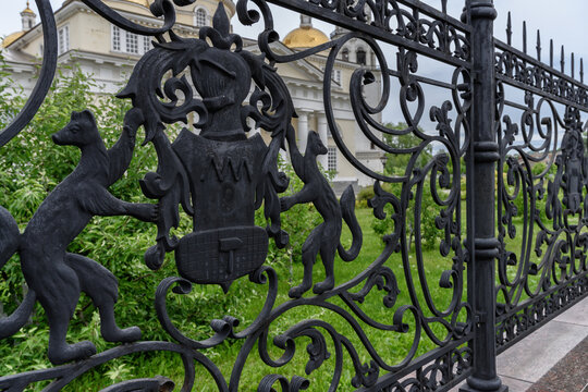 wrought iron fence grates. close-up. fine openwork work of cast iron. a fence around the historical center of the city with the image of the coat of arms of Nevyansk (Russia). summer clear day