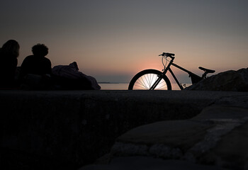 Obraz na płótnie Canvas bicycle resting on the rocks in front of the sunset over the sea