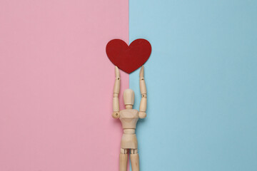 Wooden puppet mannequin holding red heart on pink blue pastel background.