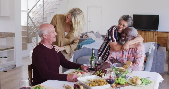 Diverse senior couples sitting by a table drinking wine eating dinner and hugging