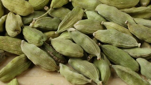 Heap of dried green cardamom pods at the background and a open one with black seeds close up