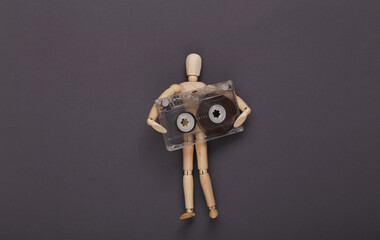 Wooden puppet mannequin holding audio cassette on gray background