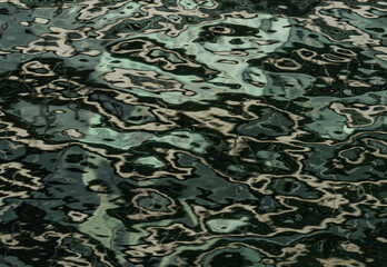 Ondas en el agua de un lago con reflejos verdes, negros y dorados