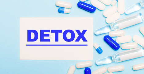 Pills, ampoules and a white card with the text DETOX on a light blue background. Medical concept