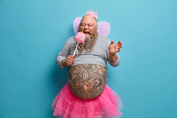 Funny bearded dad with tattooed belly entertains kids on party being holiday performer dressed like...
