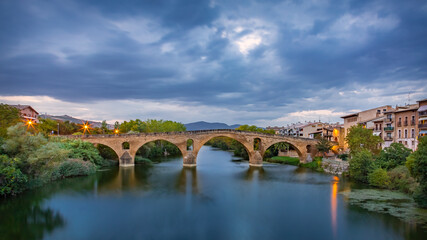 Fototapeta premium The Early Blue Hour on a Cloudy Evening over the Iconic Bridge in Puente la Reina, along the French Way of St James Camino de Santiago