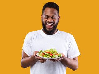 Excited African Man Holding Salad Plate Standing Over Yellow Background