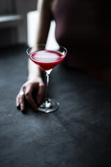 A red raspberry sour cocktail in a beautiful coupe glass in girl's hands, back light, dark and moody photo