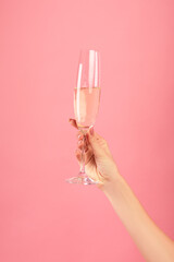 Closeup of female hand holding glass of champagne on pink studio background. Holiday celebration concept © Prostock-studio