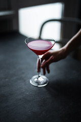A red raspberry sour cocktail in a beautiful coupe glass in girl's hands, back light, dark and moody photo