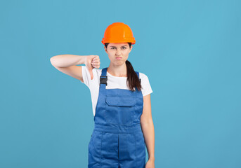 Portrait Of Young Handywoman Lady In Hardhat And Coveralls Showing Thumb Down