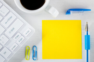 Yellow sheet of paper with space for text. Office accessories, computer keyboard, pen, coffee staples