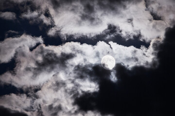 Full moon over the clouds in the night sky. Mysterious picture of the moon