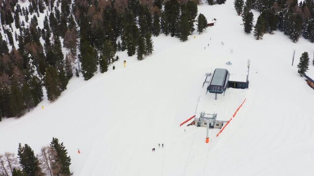 Aerial flyover closed snowy Alpe Lusia Ski Area with ski lift surrounded by conifer trees in nature. Moena,Italy.
