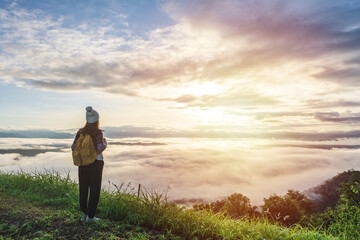 Naklejka na ściany i meble Young woman travelers looking at the sunrise and the sea of mist on the mountain in the morning, Travel lifestyle concept