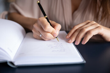 Close up businesswoman writing in notebook, planning workday, meetings, entrepreneur managing time, sitting at table, student making note during lecture, preparing for exam, handwriting