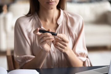 Close up unhealthy woman measuring glucose level, using lancet pen on finger, businesswoman sitting...