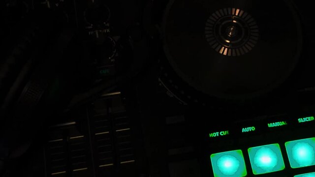 Looped Video of DJ AV mixing controller console at birds eye view perspective in dark night club setting with neon lights flashing synchronized to the music video playing with black headphone ontop