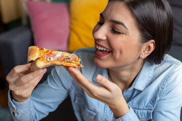 A young brunette woman is eating pizza at home.