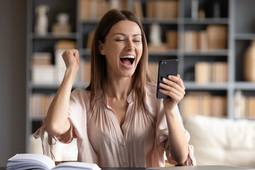 Close up overjoyed woman looking at phone screen, celebrating success, showing yes gesture, sitting...