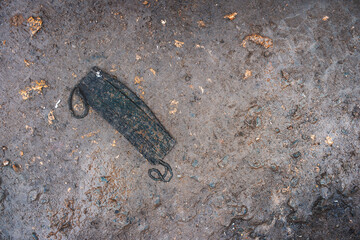 Used trampled dirty fabric face mask lying on muddy ground. Public spaces are flooded with discarded protective equipment.