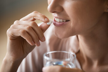 Close up smiling attractive woman holding white round pill and glass of water, happy young female...