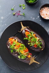 Baked stuffed eggplant with different vegetables, tomato, pepper, onion and parsley in round black plate on dark stone or concrete table background. Top view.