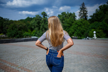 A beautiful girl with blond long hair of European appearance. Dressed in jeans and a T-shirt. Walk on a sunny day