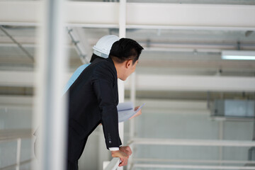 Asian engineer wearing hard hat talking with business man in formal suit in the factory