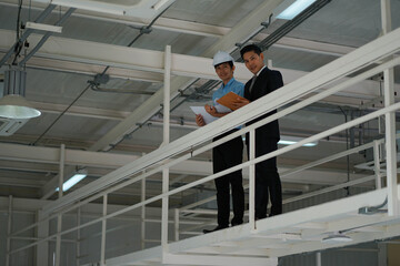 Asian engineer wearing hard hat talking with business man in formal suit in the factory
