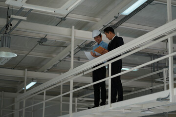 Asian engineer wearing hard hat talking with business man in formal suit in the factory