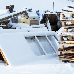 in winter, old doors stand near the house and a pile of transported wooden pallets