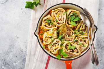 Meat dough rolls with meat or lazy dumplings in old red cast-iron pan on rustic gray background. Top view.