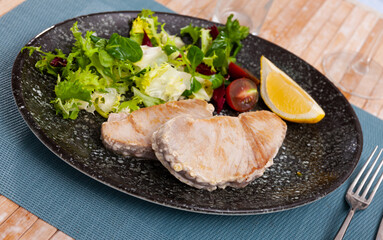 Prepared tuna steak served with lemon and tomato on plate on wooden table