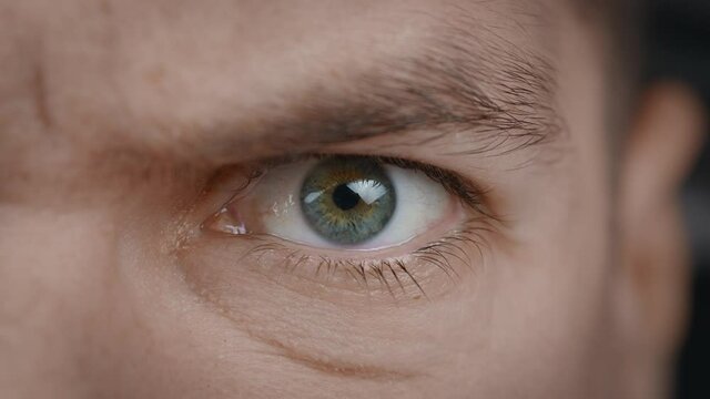 Close-up portrait of angry man's eye. Aggressive male's eyes blinking and looking seriously at camera.