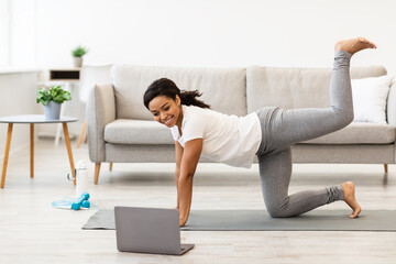 Black woman exercising at home watching tutorial on laptop - obrazy, fototapety, plakaty