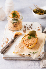Sandwich with delicious homemade chicken pate with spices and dill in a glass jar and a slice of bread nearby and caper on a light board background. Selective focus.