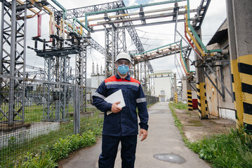 An electrical substation engineer inspects modern high-voltage equipment in a mask at the time of...