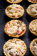 Salad tartlets with pineapple on a black wooden board on a gray concrete background.