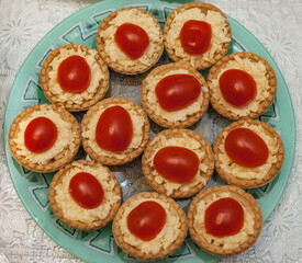 Tartlets with grated cheese with mayonnaise and tomato halves close-up on a light green plate against a white tablecloth