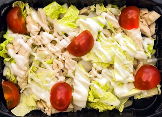 Salad of boiled chicken with fresh white cabbage, decorated with white yogurt and tomato slices close-up on a black plastic substrate