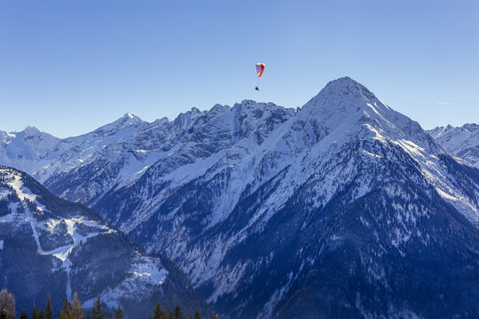 Lone paraglider above snow capped spring textured mountains