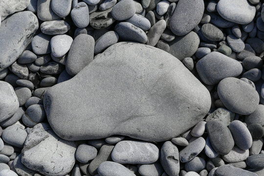 Flat grey textured stone on pebble beach with copy space