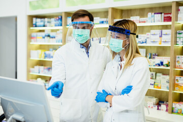 Male and female pharmacists with protective mask and face shield on their faces working at pharmacy. Medical healthcare concept.