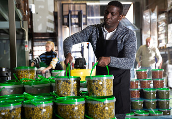 African-American man engaged in producing of pickled olives, arranging plastic buckets with finished products